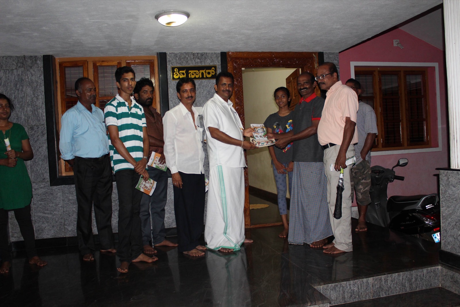 Udaya Shetty Muniyal handing a pamphlet to a family at their doorstep